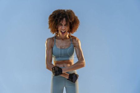 Foto de Mujer en ropa deportiva muestra sus músculos de pie en el fondo del estudio. Resultados del entrenamiento - Imagen libre de derechos