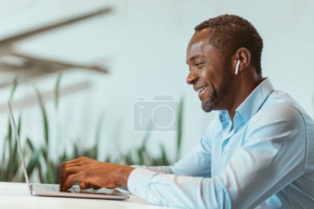Foto de Hombre de negocios africano guapo que trabaja en el ordenador portátil mientras está sentado en la oficina moderna. Foto de alta calidad - Imagen libre de derechos