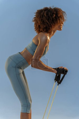 Foto de Mujer deportiva realiza ejercicios con expansor sobre fondo de estudio azul. Fuerza y motivación - Imagen libre de derechos