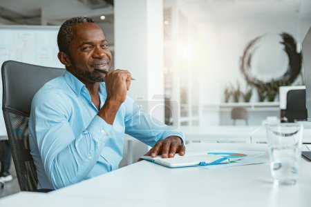 Photo for Smiling African businessman taking notes while sitting in modern office. High quality photo - Royalty Free Image