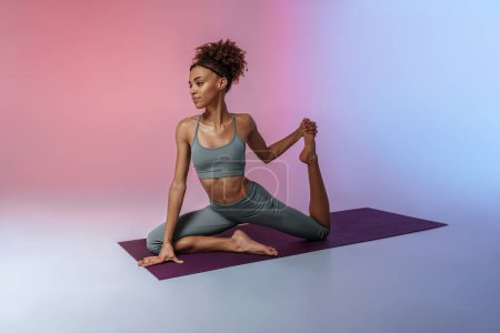 Téléchargez les photos : Athletic woman in sportswear doing stretching exercises on yoga mat on studio background - en image libre de droit