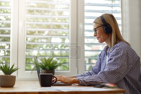Téléchargez les photos : Belle femme freelance dans les lunettes de travail sur ordinateur portable à partir du bureau à la maison. Photo de haute qualité - en image libre de droit