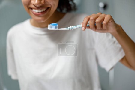 Téléchargez les photos : Femme souriante se brossant les dents devant son miroir de salle de bain. Procédure de beauté de routine du matin - en image libre de droit