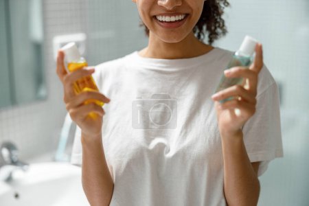 Téléchargez les photos : Femme souriante tenant des cosmétiques de soins naturels debout dans la salle de bain. Photo de haute qualité - en image libre de droit