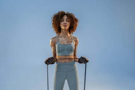 Photo for Strong woman in sportswear performs fitness exercises with resistance band on studio background - Royalty Free Image