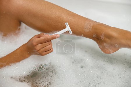 Téléchargez les photos : Vue rapprochée de la femme se rasant la jambe avec un rasoir. Procédure de dépilation à la salle de bain. Photo de haute qualité - en image libre de droit