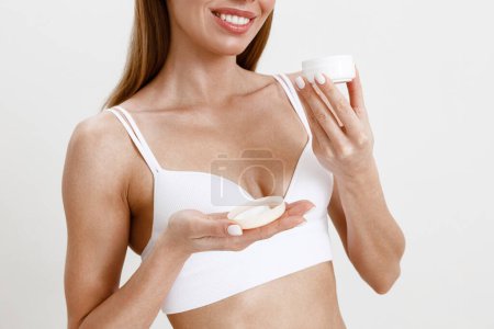 Téléchargez les photos : Femme mince méconnaissable sur fond blanc studio portant lingerie appliquer crème hydratante - en image libre de droit