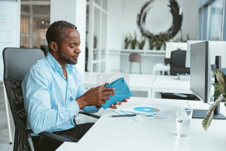 Téléchargez les photos : Homme d'affaires africain travaillant avec des documents tout en étant assis dans un bureau moderne. Photo de haute qualité - en image libre de droit
