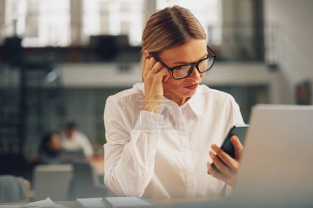 Téléchargez les photos : Focused femme responsable des ventes utilisent le téléphone pendant la journée de travail dans le bureau moderne. Photo de haute qualité - en image libre de droit