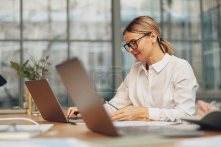 Foto de Trabajadora de oficina bastante mujer que trabaja en el ordenador portátil mientras está sentada en coworking moderno. Foto de alta calidad - Imagen libre de derechos
