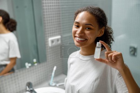 Photo for Smiling woman holding natural skincare cosmetics standing in bathroom. High quality photo - Royalty Free Image