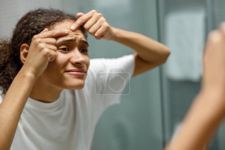 Téléchargez les photos : Femme enlever le bouton de son visage tout en regardant miroir dans la maison de salle de bains. Photo de haute qualité - en image libre de droit