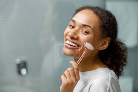 Photo for Woman making face massage using face roller with quartz stone in bathroom. High quality photo - Royalty Free Image