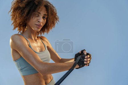 Téléchargez les photos : Femme forte en vêtements de sport effectue des exercices de fitness avec bande de résistance sur fond de studio - en image libre de droit