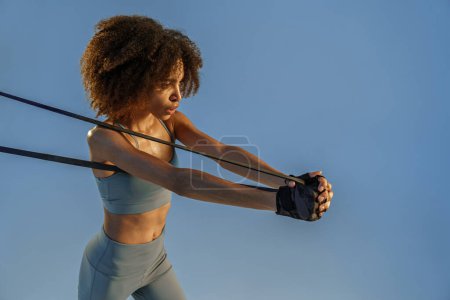Téléchargez les photos : Femme forte en vêtements de sport effectue des exercices de fitness avec bande de résistance sur fond de studio - en image libre de droit