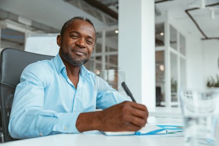 Foto de Empresario africano confiado tomando notas mientras está sentado en la oficina moderna. Foto de alta calidad - Imagen libre de derechos