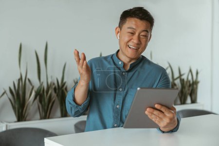 Téléchargez les photos : Homme d'affaires asiatique souriant faisant videocall à client assis dans le coworking moderne. Photo de haute qualité - en image libre de droit