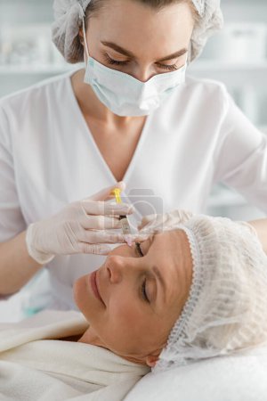 Foto de Inyección vertical de la mujer cosmetóloga que hace la inyección para madurar cliente femenino en la clínica, de cerca - Imagen libre de derechos