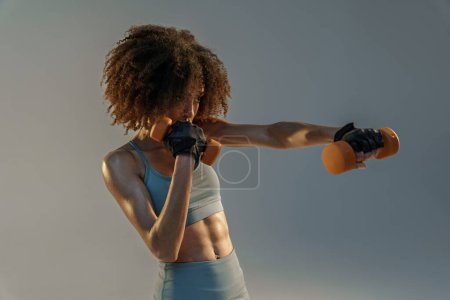 Téléchargez les photos : Femme musculaire faisant de l'exercice avec haltères de poids sur fond de studio - en image libre de droit