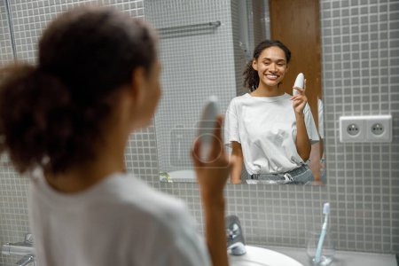 Photo for Woman holding antiperspirant and smiling standing in bathroom. Body care concept. High quality photo - Royalty Free Image