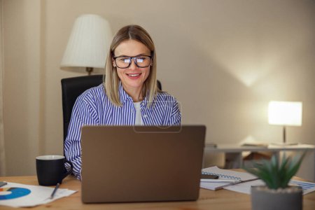 Téléchargez les photos : Belle femme freelance dans les lunettes de travail sur ordinateur portable à partir du bureau à la maison. Photo de haute qualité - en image libre de droit
