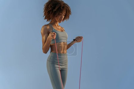 Foto de Mujer deportiva en ropa deportiva sosteniendo la cuerda de salto en el fondo del estudio. El mejor entrenamiento cardiovascular - Imagen libre de derechos