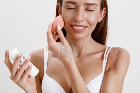Téléchargez les photos : Jeune femme tenir éponge rose pour l'application de produits cosmétiques de beauté sur le visage. Photo de haute qualité - en image libre de droit