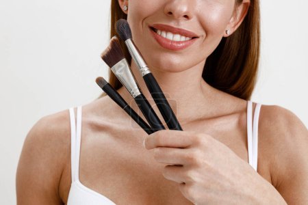 Téléchargez les photos : Jeune femme avec une peau saine maquillage à l'aide d'une brosse cosmétique sur fond de studio - en image libre de droit