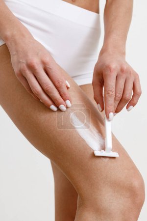 Foto de Primer plano de la mujer afeitándose la pierna usando navaja de afeitar sobre fondo blanco del estudio. Foto de alta calidad - Imagen libre de derechos