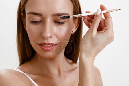 Foto de Mujer joven peinándose las cejas con cepillo de frente sobre fondo blanco del estudio. Maquillaje de pesca - Imagen libre de derechos