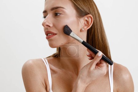 Foto de Mujer joven con piel sana haciendo maquillaje usando cepillo cosmético en el fondo del estudio - Imagen libre de derechos