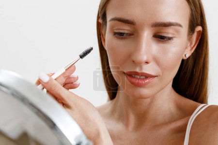 Foto de Mujer joven peinándose las cejas con cepillo de frente sobre fondo blanco del estudio. Maquillaje de pesca - Imagen libre de derechos