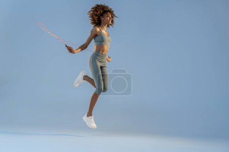 Foto de Vista lateral de la mujer saltando con cuerda de salto en el fondo del estudio. El mejor entrenamiento cardiovascular - Imagen libre de derechos