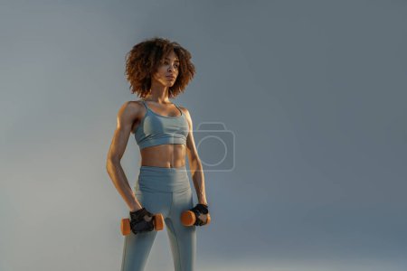 Téléchargez les photos : Femme faisant des exercices avec haltères sur fond de studio et regardant côté - en image libre de droit