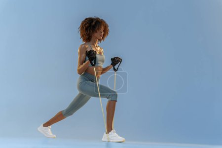 Téléchargez les photos : Vue latérale de la femme effectue des exercices avec extenseur sur fond de studio. Force et motivation - en image libre de droit