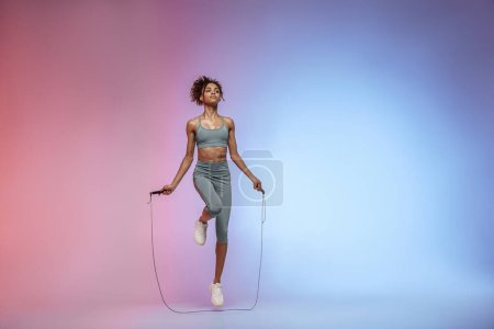 Téléchargez les photos : Femme sauter avec corde à sauter sur fond de studio avec filtre de couleur. Meilleur entraînement cardio - en image libre de droit