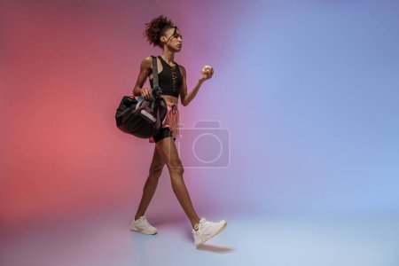 Foto de Mujer que va a entrenar con botella de agua, bolsa de deporte y manzana contra fondo de estudio - Imagen libre de derechos