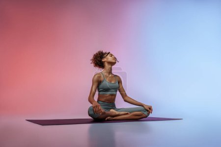 Téléchargez les photos : Fitness femme pratiquant le yoga sur tapis sur fond de studio avec filtre de couleur. Photo de haute qualité - en image libre de droit