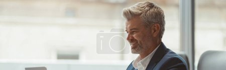 Photo for Smiling Mature businessman workingon laptop while sitting in modern coworking. High quality photo - Royalty Free Image