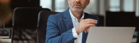 Téléchargez les photos : Homme d'affaires mature occupé travaillant sur ordinateur portable tout en étant assis dans le coworking moderne. Photo de haute qualité - en image libre de droit