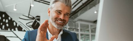 Photo for Smiling businessman talking online with client sitting in modern office. Blurred background - Royalty Free Image