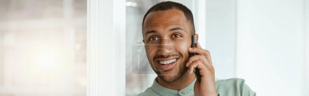 Photo for Smiling african businessman talking phone with client while standing in office. Blurred background - Royalty Free Image