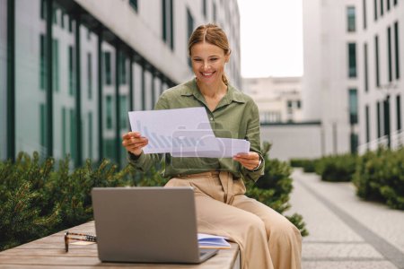 Téléchargez les photos : Femme gestionnaire travaillant avec des documents et utiliser un ordinateur portable assis à l'extérieur du bureau - en image libre de droit