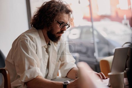 Téléchargez les photos : Focalisé freelance masculin travaillant sur ordinateur portable tout en étant assis dans le coworking moderne. Photo de haute qualité - en image libre de droit