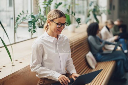 Foto de Mujer gerente trabajando en el ordenador portátil en coworking moderno mientras está sentado cerca de la ventana. Foto de alta calidad - Imagen libre de derechos