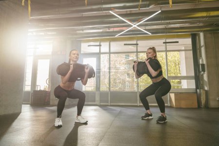 Téléchargez les photos : Groupe de femmes athlétiques En classe d'aérobic effectuant des exercices de squat sac dans la salle de gym. Photo de haute qualité - en image libre de droit