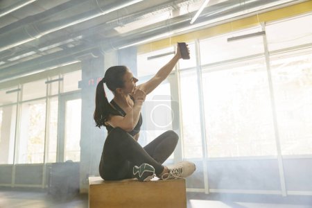 Téléchargez les photos : Ajustez femme en vêtements de sport prendre un selfie après l'entraînement dans la salle de gym pendant le repos. Photo de haute qualité - en image libre de droit
