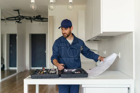 Foto de Reparador en uniforme de pie en la cocina con el plan de casa antes de comenzar a trabajar. Foto de alta calidad - Imagen libre de derechos