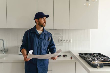 Foto de Hombre trabajador en uniforme de pie en la cocina con el plan de casa antes de comenzar a trabajar. Foto de alta calidad - Imagen libre de derechos