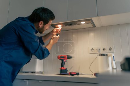 Photo for Professional male worker in uniform repairing modern cooker hood in kitchen. High quality photo - Royalty Free Image